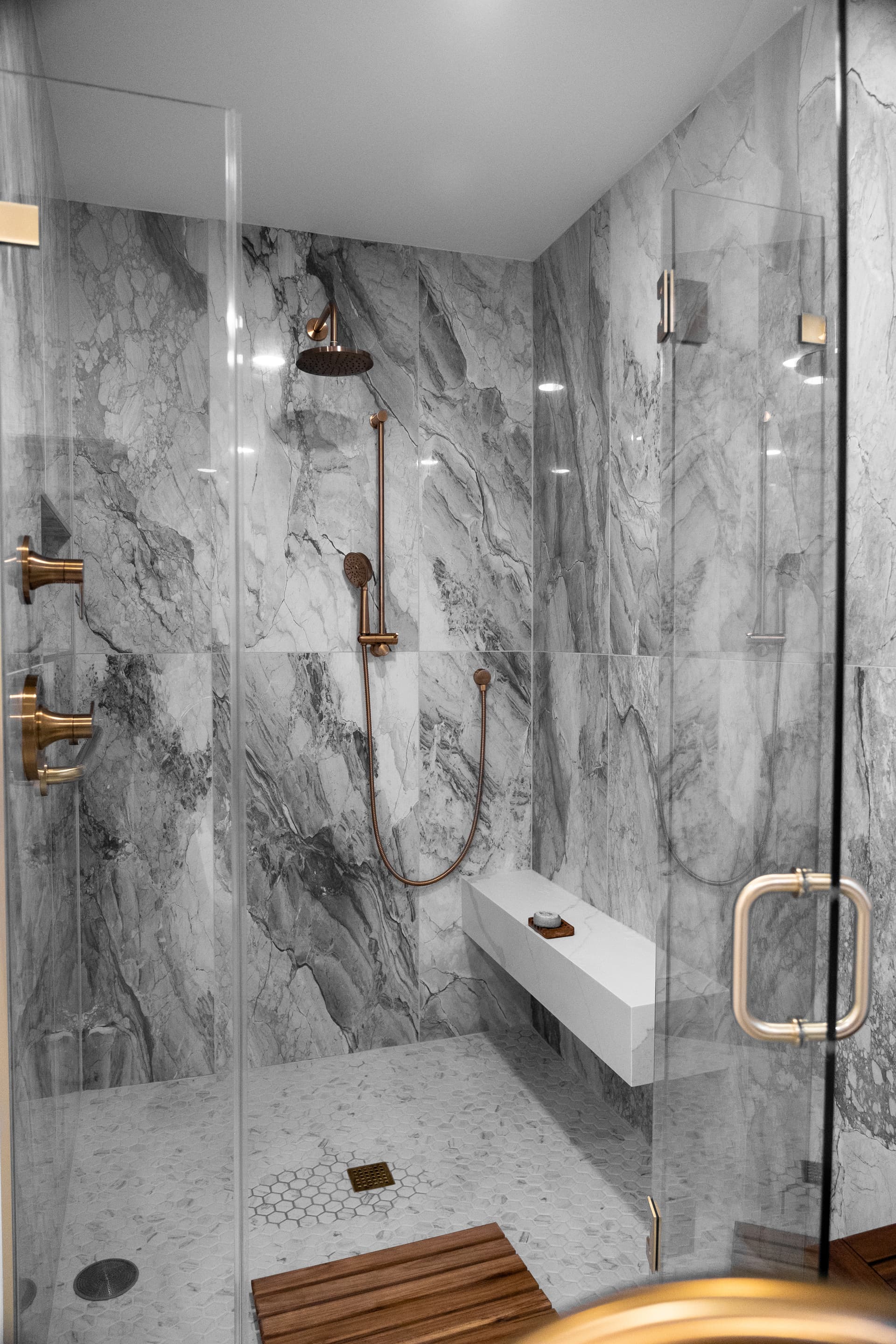 Walk-in marble shower with brass fixtures and floating bench